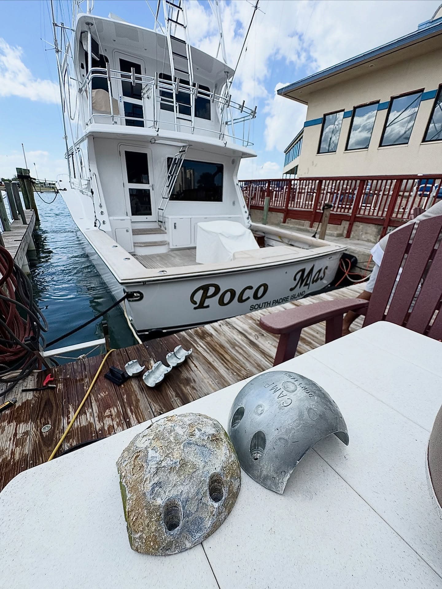 Sportfishing boat Poco Mas docked behind two removed marine anodes displayed on a table.