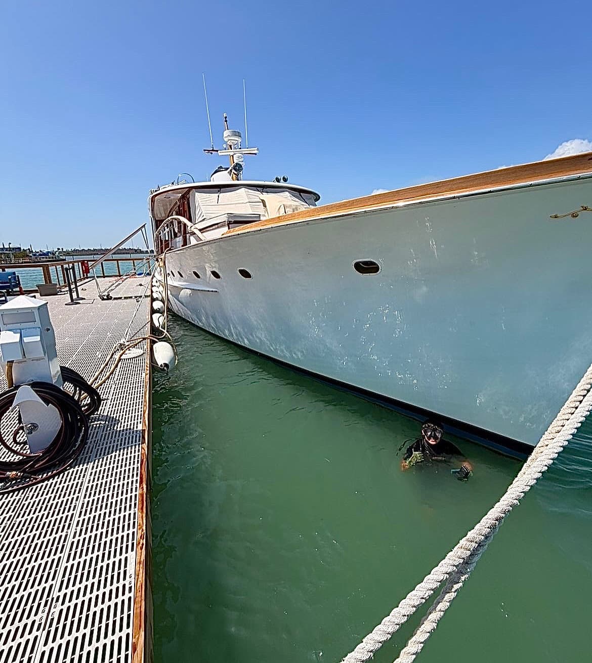 A diver works in the water alongside a large yacht at the dock.